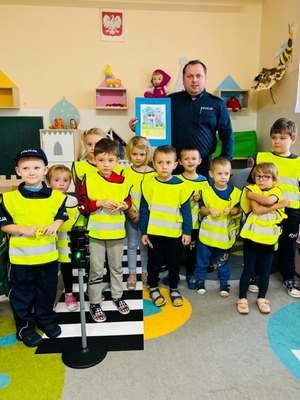 asp. Dawid Mucha trzymający dyplom od dzieci, stojący razem z nimi